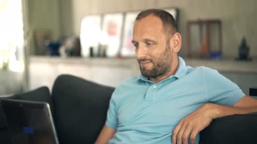 Man relaxes on couch, using laptop at home