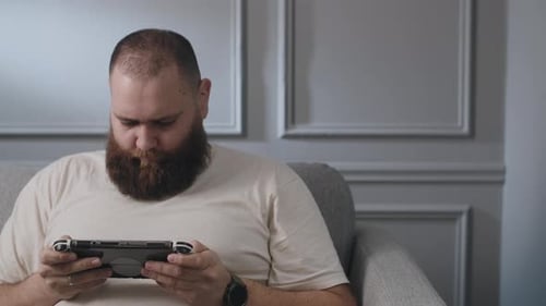 Man Playing Handheld Video Game Console on Couch
