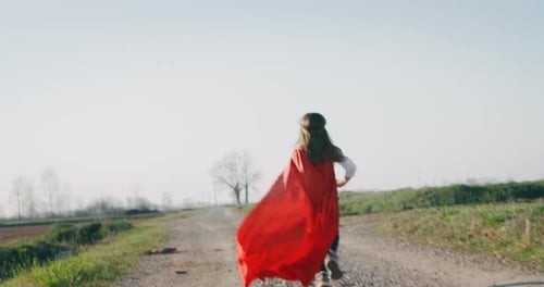 Authentic shot of a funny little girl dressed as superhero in red cape running and having fun on a