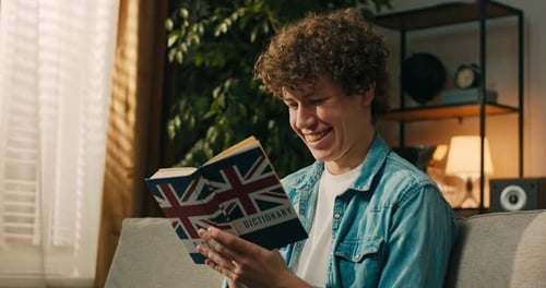 A Focused Smiling Student Boy Holds Up an English Dictionary and Repeats New Vocabulary Words in His