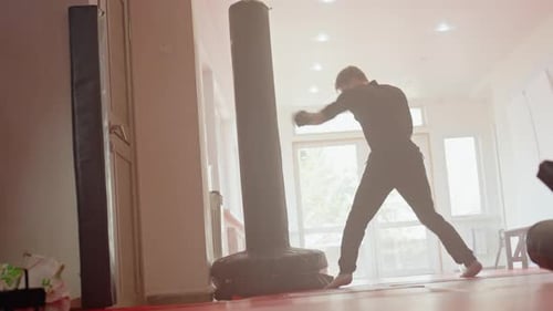 Athlete in Gym Wearing Gloves Practices Boxing Drills Against Punching Bag