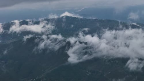 Aerial drone shot capturing a surreal view of layered mountains under a cloud-filled morning sky.
