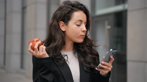 Woman Eats Apple and Checks Phone in City