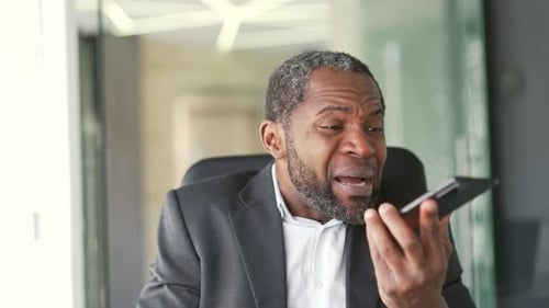 Close up. Angry mature african american man in formal suit talking and arguing on smartphone while s