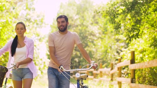Conceito de pessoas, lazer e estilo de vida - jovem casal feliz com bicicletas caminhando