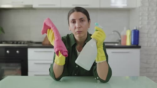 Erschöpfte Hausfrau in gelben Handschuhen sitzt am Küchentisch