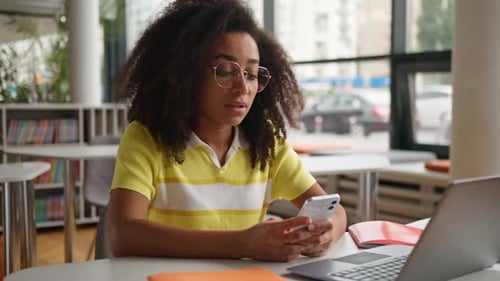 Young Woman Using Phone at Desk with Laptop