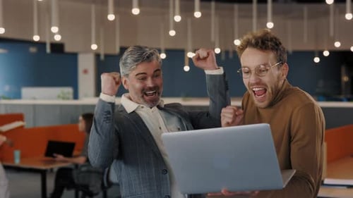 Two Male Colleagues Using Laptop and Looking Happy When Getting Good News Standing in the Office