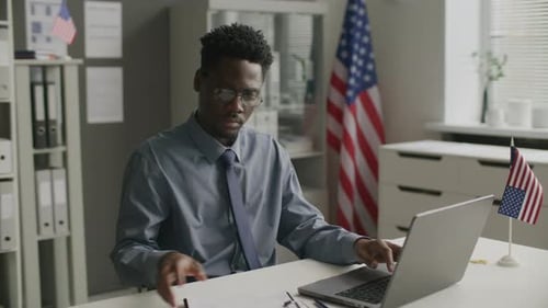 African American Visa Officer Working on Laptop at Desk in US Embassy