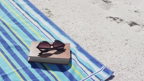 Video of sunglasses, book, towels and beach equipment lying on beach