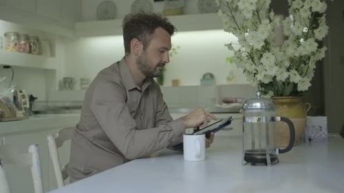 Man uses tablet at kitchen table with coffee