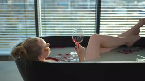 Spa Relaxation Woman Lying in Bath with Holding Glass with Red Wine Girl Relaxing in Bathroom at