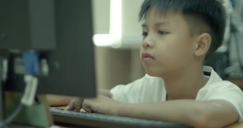 An Asian boy in elementary school is having fun using his desktop computer to play games