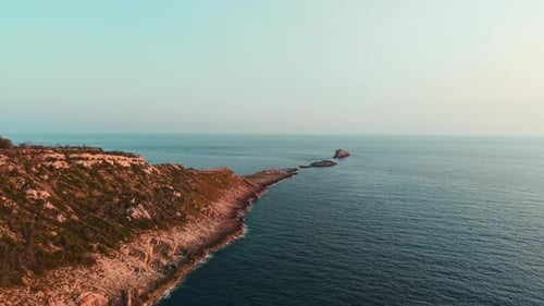 Mediterranean Coastline Extending Toward Rocky Islet During Golden Sunset Glow