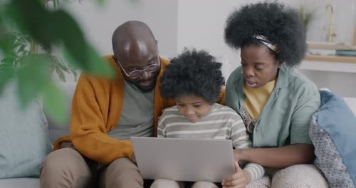 Happy African American Child Using Laptop Computer and Talking to Parents Mother and Father Sitting
