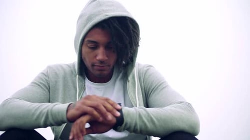 Young man with dreadlocks resting in sunlight after exercise on foggy meadow