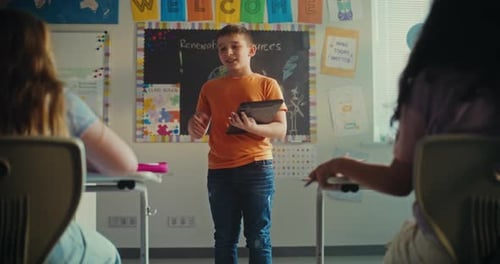 Elementary School Boy with Tablet Computer Presenting Homework on Ecology in Front of Classmates