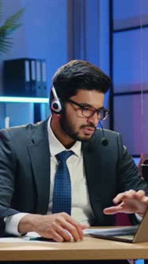 Man in Suit Wearing Headset Working on Laptop