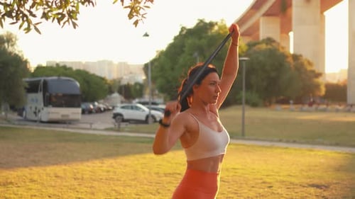 Sporty Woman Exercising with Resistance Band at Park During Sunny Day