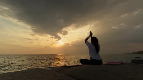 Woman Practicing Yoga Meditation at Ocean Sunset by the Sea