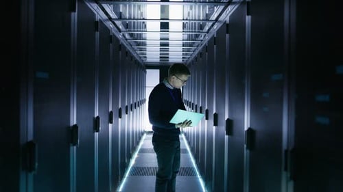 Un
ingeniero de TI masculino trabaja en una computadora portátil en un centro de Big Data. Se ven filas de servidores en rack.