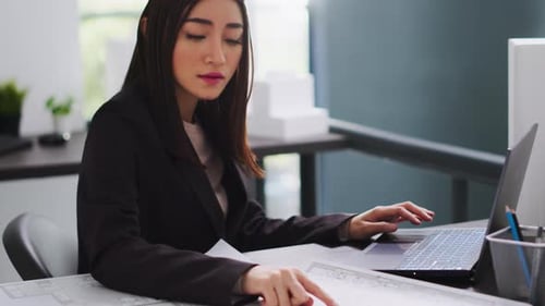 Asian Architect Translating Floor Plan Measurements on Laptop
