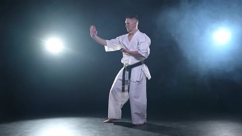 Starker Kämpfer im weißen Kimono für Karate-Kampfkünste mit schwarzem Gürtel bereitet sich auf den Kampf vor
