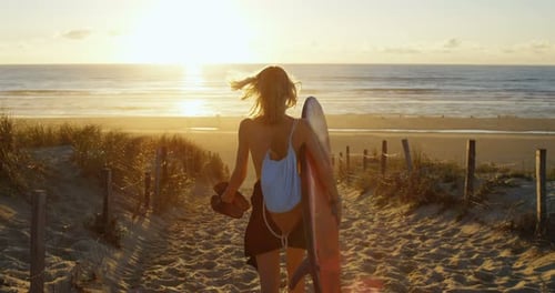 Beautiful Young Woman in a Swimsuit Holding Surfboard Walks on the Beach Towards the Sea. Sun Shine