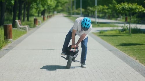 Man Preparing to Ride Electric Unicycle on Park Path Under Sunny Sky