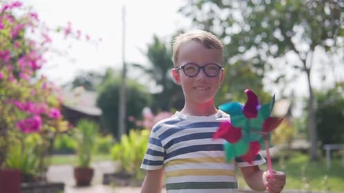 Boy in glasses is playing with pinwheel in a garden