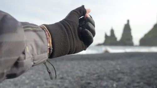 close up hand with glove, falling black sand on black sand beach in Iceland.