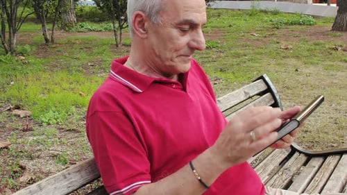 Retired senior man resting and using his tablet at table in park