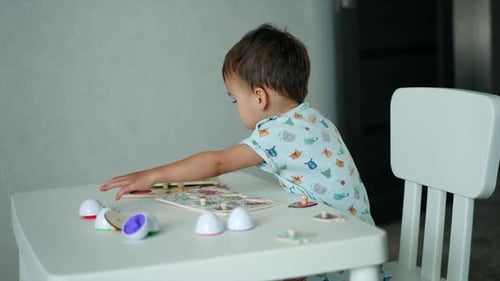 Lovely child sitting at the desk with toys on it. Little kid is focused on his game with puzzles.