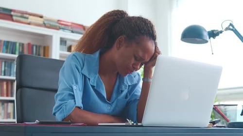 Junge unglückliche Afroamerikanerin schaut sich Laptop an, der am Bürotisch sitzt