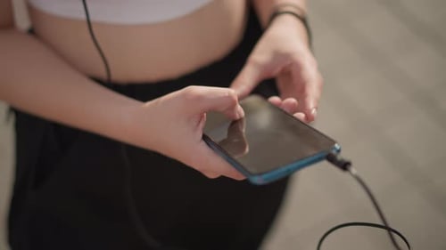 Young Woman Plugs Headphones into Smartphone