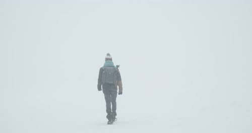 Person with backpack hiking on snowy mountain during snowstorm and hiding