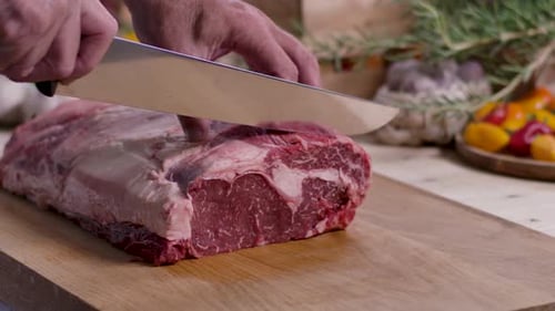 Raw Beef Being Cut Into Steaks on Wood