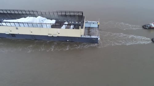 Three tugboats pulling heavy industrial barge with white cargo