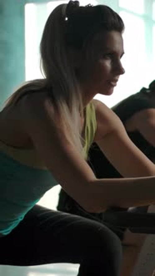 Vertical of Athletes Train the Muscles of the Legs on the Exercise Bike in the Gym in a Row