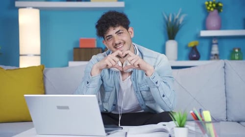 Smiling Man Makes Heart Shape with Hands at Laptop