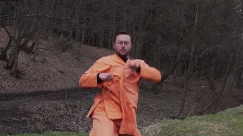 Caucasian Karateka In Orange Yi-fu Practicing Kung Fu In The Forest. medium shot