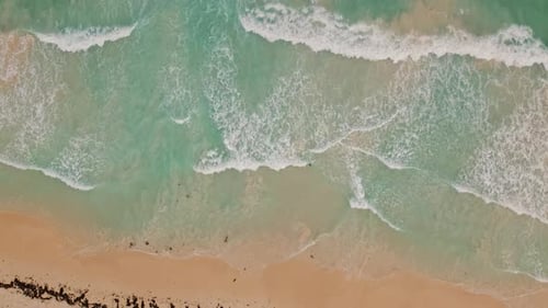 Aerial top down view of sea waves crashing onto a wide sand beach in slow motion