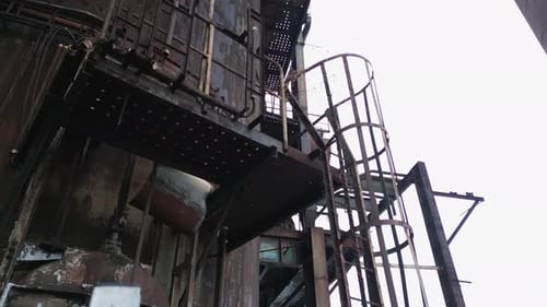 Abandoned and rusted industrial structure with a spiral staircase attached to its side. Eerie atmosp