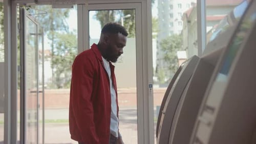 Ernster gutaussehender junger Mann steckt Kreditkarte in Bancomat und gibt eine PIN ein, um Geld zu erhalten