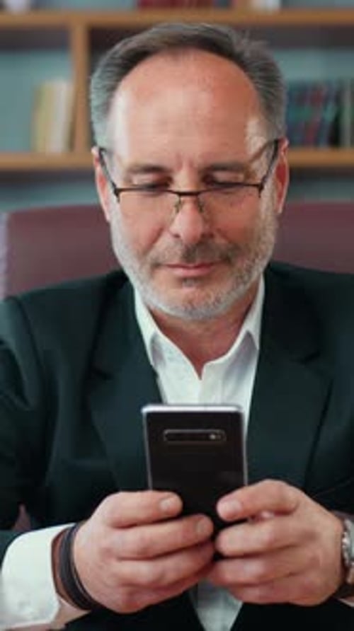 Goodlooking Confident Smart Adult Bearded Manager Sitting at His Workplace and Using His Smartphone
