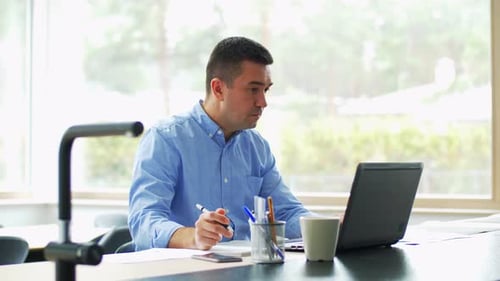 Man working on laptop, writing in a notebook