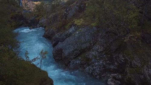 Drone panning over a small creek, flying up and revealing beautiful scenic view of a waterfall comin