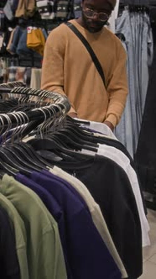 Vertical of Man Looking for Right Size of Plain T-Shirt in Clothing Shop
