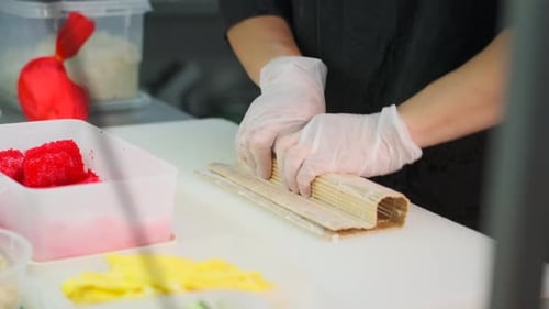 Sushi chef wrapping a roll using a bamboo sushi mat on kitchen table. Close-up.