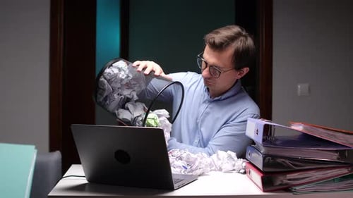 Frustrated Office Worker Emptying Wastebasket on Laptop Keyboard